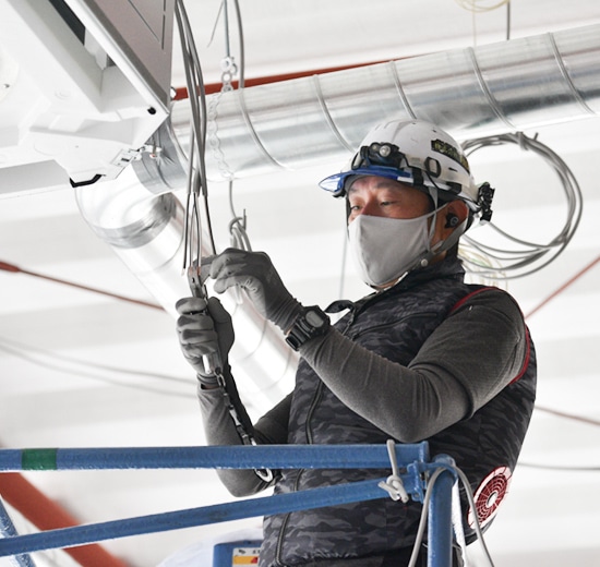 ヘルメットを着用し、天井の電気配線工事を行う作業員