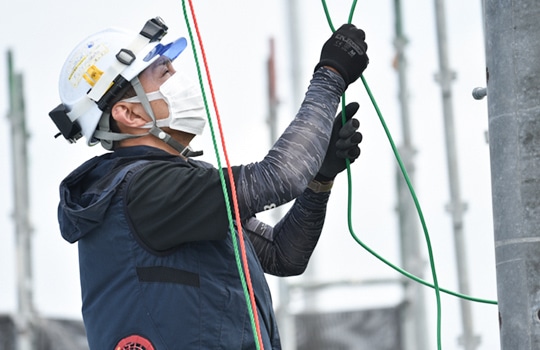 ヘルメットと空調服を着用し、屋外で配線作業を行う作業員